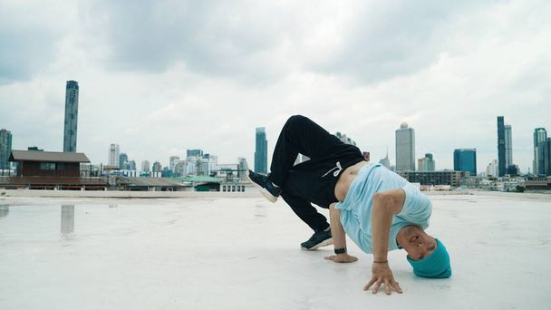 Danseur B-boy caucasien pratiquant la danse de rue sur le toit avec la ville ou urbaine. Prise de vue en mouvement d'un jeune homme dansant dans la rue en posant sur le gel ou en se tenant debout. Sport de plein air 2024. Endeavor. - Photo, image