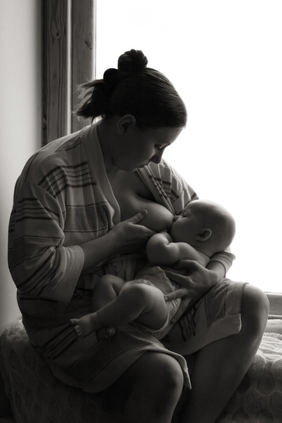 Mulher amamentando perto de uma janela, bebê cochilando, preto e branco
 - Foto, Imagem