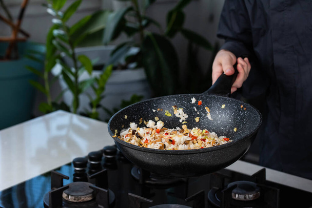 Großaufnahme der Hände des Chefkochs beim Kochen von gebratenem Gemüse mit Reis für die asiatische Küche in der Wokpfanne auf Gasherd. - Foto, Bild