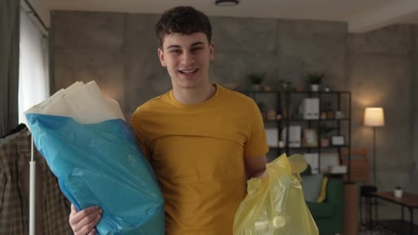 Ein junger Mann recycelt zu Hause Altpapier und Glas zu grünen, gelben und blauen Säcken - Filmmaterial, Video