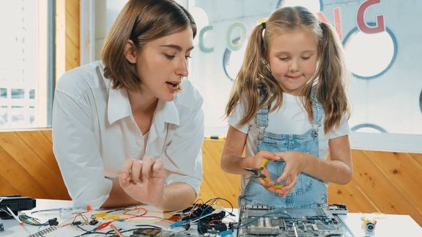 Young smart caucasian teacher teaching students about part of electronic board. Expert girl learn about digital electrical tool and fixing motherboard at table with chips and wires placed. Erudition. - Photo, Image