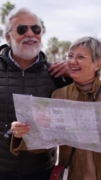 Vertikální starší Kavkazský turistický pár s úsměvem drží cestovní mapu a hledí společně na zajímavá místa. Starší manžel a manželka procházející se po ulici a užívající si dovolenou důchodců. Dospělí turisté  - Záběry, video