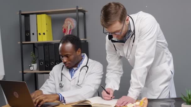 Médicos varones trabajando juntos en el ordenador portátil de la clínica - Metraje, vídeo
