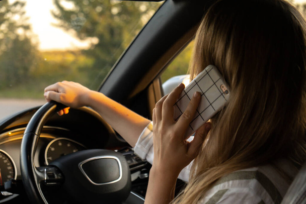 Happy young woman speaking by mobile phone while driving car. Business woman talking phone call in automobile. Unsafely risky driving. Concept of multitasking  - Photo, Image