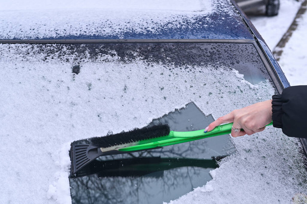 το χέρι μιας γυναίκας με ξύστρα αφαιρεί τον πάγο από το παράθυρο του αυτοκινήτου - Φωτογραφία, εικόνα
