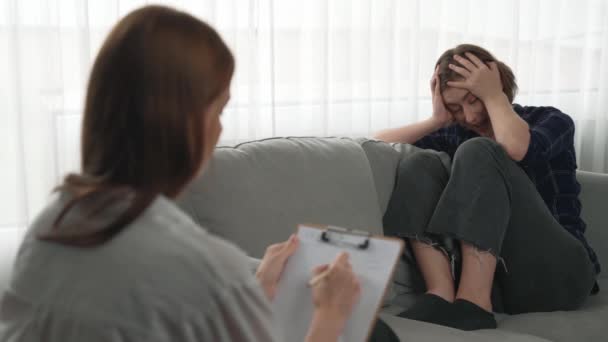 悲しいPTSDの女性は,心理学者,うつ病,または人生の失敗後の悲しみの精神的健康のための治療を受けています. 診療所での感情についての主要な心理学者と話す疲労したトラウマの若い女性 - 映像、動画