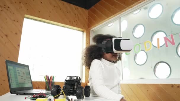 Luova onnellinen tyttö VR-kuulokkeissa ja katselee ympärilleen metavernassa. Hauska lapsi nauttii pääsystä virtuaalimaailman ohjelmaan STEM-teknologialuokassa, jossa on automalli ja pöydälle asetetut johdot. Virheellisyys. - Materiaali, video
