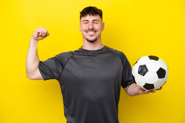 młody piłkarz człowiek odizolowany na żółtym tle robi silny gest - Zdjęcie, obraz
