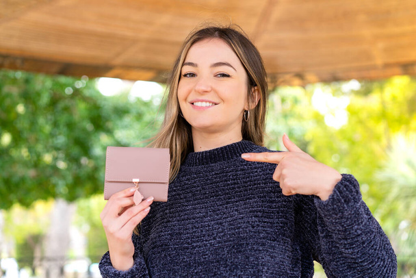 Jovem mulher romena bonita segurando uma carteira ao ar livre e apontando-o - Foto, Imagem