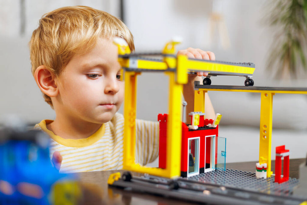 Een jonge jongen is sterk gericht op het bouwen van een structuur met een speelgoed bouwpakket, met de nadruk op zijn concentratie en creativiteit. - Foto, afbeelding