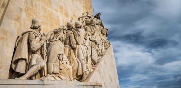 Widok z dołu zachodniego profilu pomnika z wapiennymi rzeźbami do odkryć w Lizbonie, Portugalia, pod zachmurzonym błękitnym niebem z poziomą przestrzenią do kopiowania. - Zdjęcie, obraz