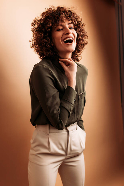 Mulher adulta rindo enquanto posando elegantemente em um fundo bege. - Foto, Imagem