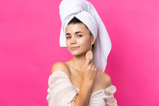 Bella ragazza attraente allegra con un asciugamano sulla testa, tiene una spugna su uno sfondo rosa. - Foto, immagini