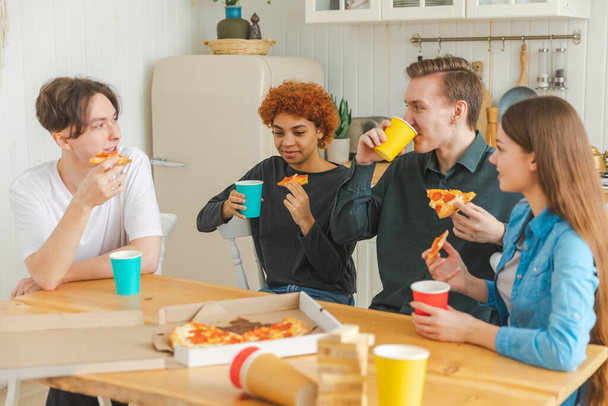 ホームパーティー。友達と一緒に家でコミュニケーションを笑って楽しい時間を過ごしています。ピザを飲むビールやレモネードを食べる幸せな多様なグループ。混合レースの若い仲間最高の友人は週末を楽しんで - 写真・画像