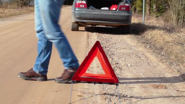 Hombre caminando cerca de triángulo de advertencia en la carretera cerca de coche
 - Metraje, vídeo