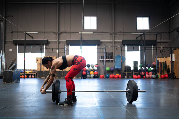 Horizontal photo with copy space of a fit woman preparing bar and lifts to weightlifting in a cross training gym - Photo, Image