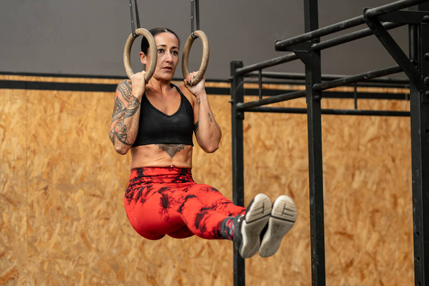 Woman performing core exercises hanging from olympic rings in a cross training gym - Photo, Image