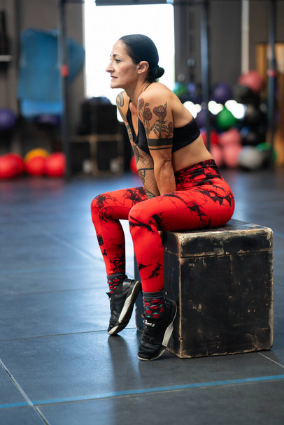Vertical photo of a relaxed mature sportswoman sitting on a box in the gym - Photo, Image