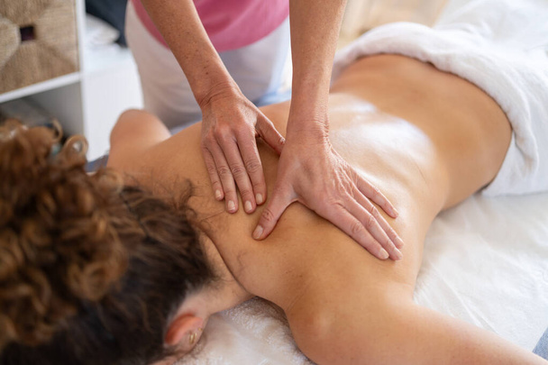 Hoge hoek van gewas anonieme massage therapeut wrijven rug van vrouwelijke patiënt liggend op de bank tijdens fysiotherapie behandeling - Foto, afbeelding