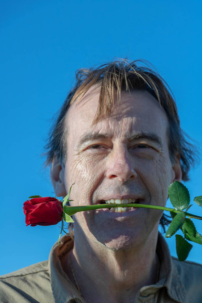 Man holding a red rose between his teeth to play young first - Photo, Image