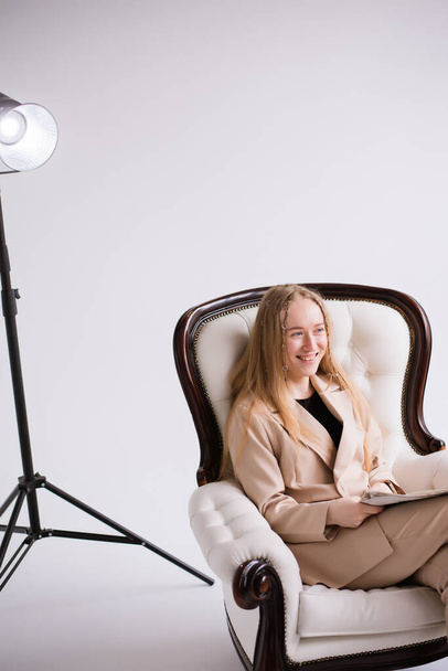 Mujer, modelo, blogger, rubia sentada en una silla en un estudio de fotografía en blanco, aislada. Vestido con un traje de pantalón beige formal - Foto, imagen
