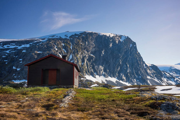 Sníh zakryl Breiddalen Valley v Jotunheimen National Park v Norsku, podél trasy do Geirangeru, během letního dne. Chata leží blízko úpatí hory..  - Fotografie, Obrázek