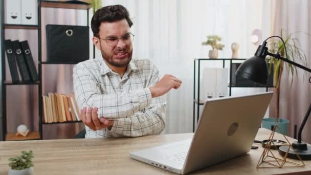 Hombre de negocios árabe indio cansado gerente sentado en el escritorio de la oficina en casa con el ordenador portátil y experimentar dolor y malestar en la articulación del codo y el masaje de la mano dolorosa. Conceptos de artritis y bursitis. - Metraje, vídeo
