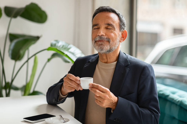 A contented mature man savoring a cup of espresso, man enjoying a coffee in modern cafe, office, enjoy break spare time and fresh drink. Positive lifestyle, morning routine - Photo, Image