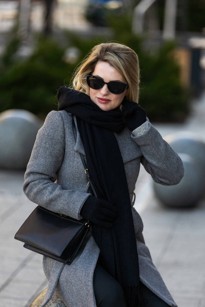Menina loira bonita nova no casaco com uma bolsa preta caminha pelo inverno e cidade da primavera. Foto de alta qualidade - Foto, Imagem