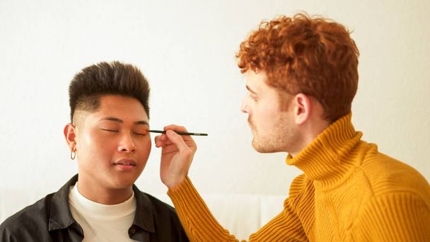 Skoncentrowany gej człowiek zastosowanie makijaż dla jej partner w domu - Zdjęcie, obraz