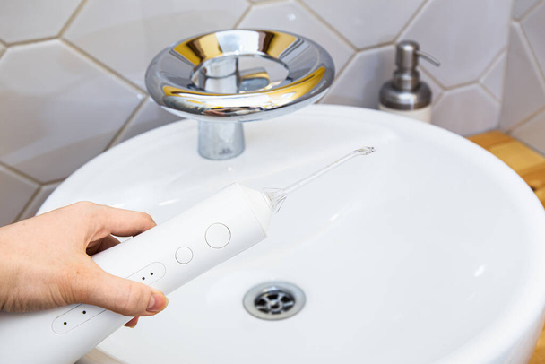 Χειροκίνητη συσκευή ενεργοποίησης νερών με πίδακα νερού σε κομψό μπάνιο, με έμφαση στην καθαριότητα και φροντίδα του στόματος. - Φωτογραφία, εικόνα