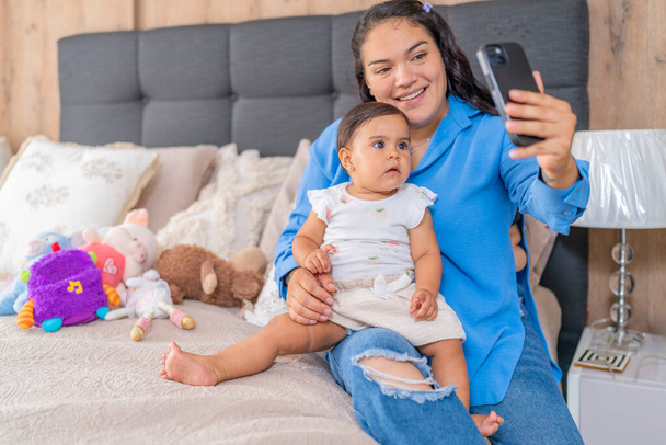 Una madre cattura un momento prezioso con il suo bambino su un letto accogliente, entrambi godendo di una sessione di selfie. - Foto, immagini