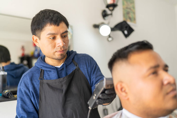 Koncentrált borbély borotválja az ügyfél haját elektromos borotvával egy borbélyüzletben - Fotó, kép