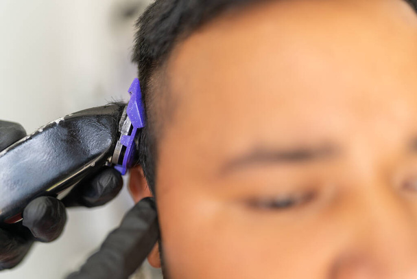 Primer plano de una afeitadora eléctrica afeitando el cabello de un cliente en una peluquería - Foto, imagen