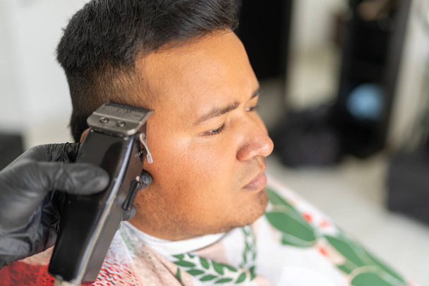 Peluquero usando afeitadora eléctrica para recortar con precisión el cabello de un cliente - Foto, imagen
