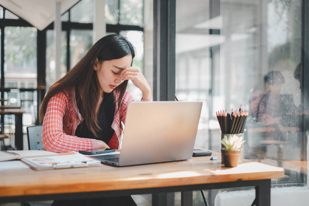 Concepto de análisis de negocios, Una mujer joven aparece estresada mientras trabaja intensamente en su computadora portátil en un escritorio de madera, rodeado de suministros de oficina - Foto, imagen