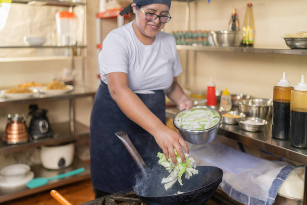 Cuoca sorridente che aggiunge verdure a una padella nel ristorante - Foto, immagini