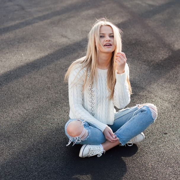 Young pretty fashionable blonde woman dressed in ripped jeans and white sweater - Фото, изображение
