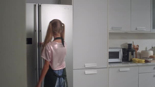Μέτριο μήκος του Καυκάσου έφηβος κορίτσι λαμβάνοντας γάλα από το ψυγείο για το μαγείρεμα στην κουζίνα - Πλάνα, βίντεο
