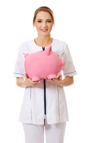 Young female doctor holding a piggybank. - Foto, immagini