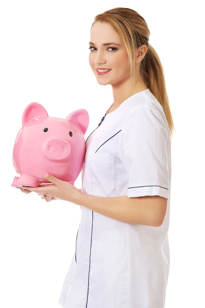 Young female doctor holding a piggybank. - Fotó, kép