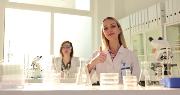 Tecniche donne felici mostrano pollici in alto nel laboratorio chimico rallentatore. Studenti sorridenti lavorano nel laboratorio universitario di medicina. Test di biochimica - Filmati, video