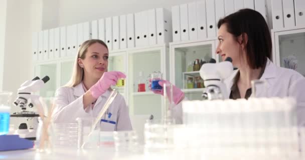 Mulheres cientistas clink copos cheios de reagentes coloridos para brincadeira antes de teste importante de líquidos especiais. Colegas trabalhando alegremente em laboratório - Filmagem, Vídeo