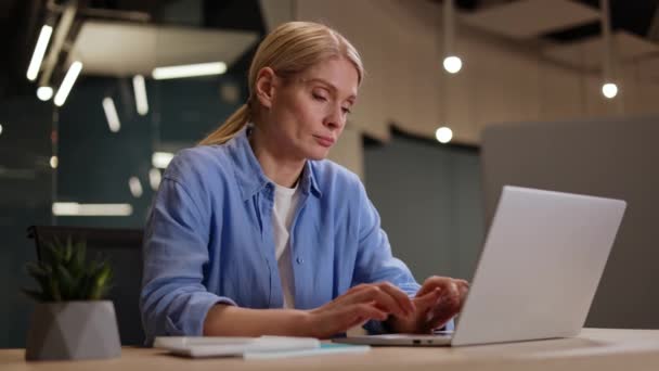Atrakcyjna kobieta w luźnych ciuchach, pracująca na laptopie i zmęczona nudną pracą w biurze. Menedżer bez motywacji pisze powoli na komputerze i czeka na koniec dnia roboczego. - Materiał filmowy, wideo