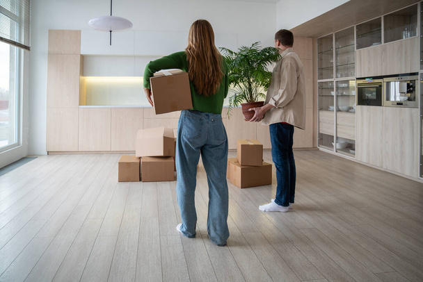 Hátsó nézet az új tulajdonosok dobozok és a szobanövény a kezében. A család elviszi a dolgokat egy másik bérelt könnyű lakásba. Házavató a jelzálog lakásban. A boldog házasélet kezdete. - Fotó, kép