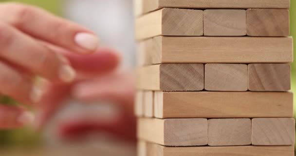 Gambler in entertaining game of Jenga takes piece of treated wood from tall tower to start game for merry friends. Starting game of Jenga - Footage, Video