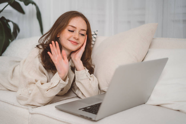 Chica pelirroja sonriente feliz usando el ordenador portátil en la sala de estar en casa, viendo videos divertidos, aprendiendo el idioma, videollamadas, madre trabajando en línea - Foto, imagen