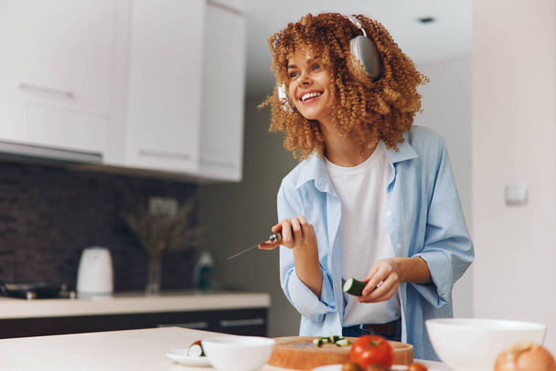 Mujer con cabello rizado cortando verduras en la tabla de cortar en el medio de la cocina para una preparación de comida saludable - Foto, Imagen