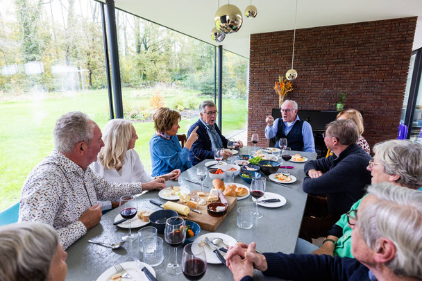Tato poutavá fotografie zachycuje rodinu, jak si užívá příjemnou snídani v moderní jídelně, která se díky oknům od podlahy ke stropu hladce mísí s venkovním prostředím. Rozložení na stole zahrnuje - Fotografie, Obrázek
