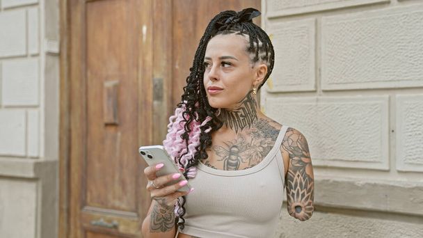 Cool hispanic geamputeerde vrouw serieus geconcentreerd op haar smartphone in stedelijke straat - Foto, afbeelding